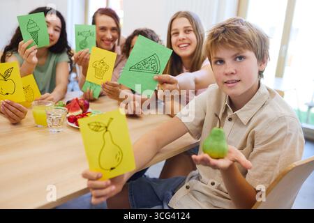 A group of students engaged in an activity, holding cards with food drawings in a school cafeteria. Stock Photo
