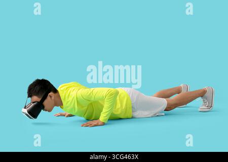 Sporty young Asian man in VR glasses doing push-ups on blue background Stock Photo