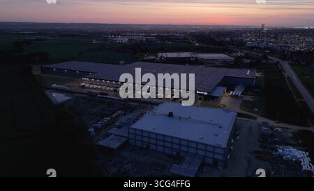 Aerial sunset panorama of a massive industrial warehouse complex and logistics hub at twilight, featuring illuminated loading docks and smart city inf Stock Photo