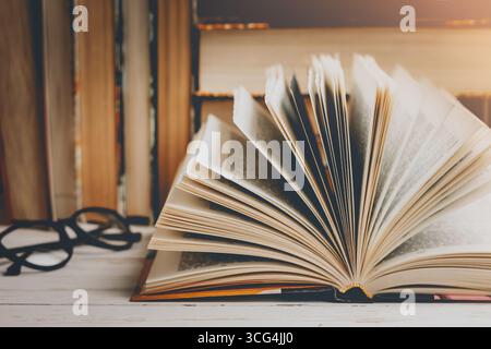 An open book with glasses on a wooden table against the background of a set of books, vintage toning. Literature, learning concept Stock Photo