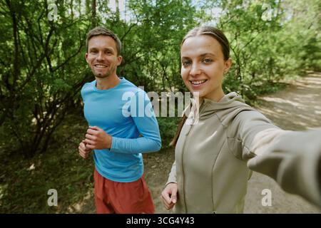 Portrait of Caucasian Young Man and Woman Jogging Together in Forest Outdoors Stock Photo