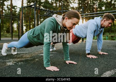 Young Caucasian Woman and Man Exercising Outdoors Performing Push Ups Together Stock Photo