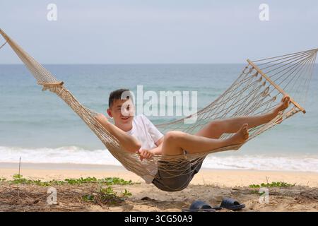 Asian man smiling on hammock by the beach in Sanya, Hainan, China Stock Photo