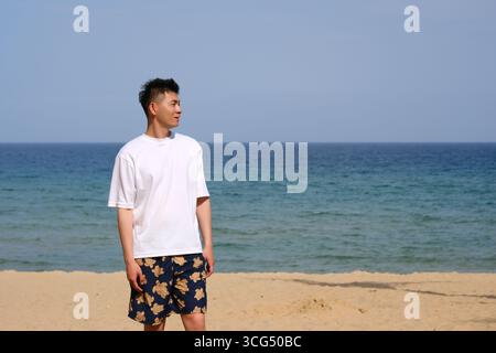 Asian young man looking at ocean on sunny beach in Sanya, Hainan, China Stock Photo