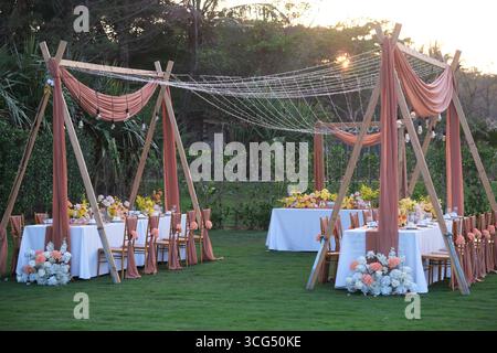 Elegant outdoor wedding dinner setup on a lawn decorated with pink drapes and wooden frames at dusk Stock Photo