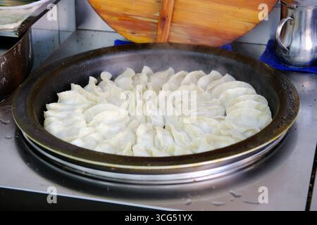 Close-up of potstickers arranged neatly in a large flat frying pan with steam rising Stock Photo