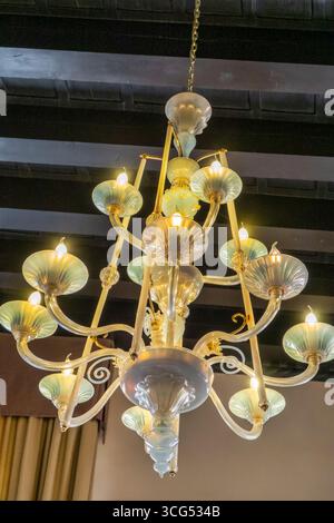 refined blown glass chandelier with golden details, hanging from a dark wooden beam ceiling. The glowing lights softly illuminate the room, creating a Stock Photo