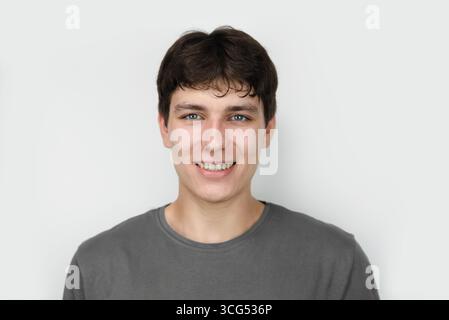 Portrait of a young man dressed in a gray shirt, smiling warmly against a light background. The guy has dark curly hair and white healthy teeth Stock Photo