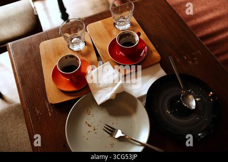 Empty plates with crumbs, cups of coffee, and glasses of water on a wooden cafe table after dessert. Top view. Stock Photo