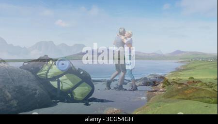 Standing mature couple embracing on wet sandy lakeshore, with lime green backpack nearby Stock Photo