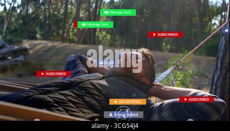 Relaxing man wearing puffer vest over plaid shirt in pine rope hammock, with floating UI badges Stock Photo