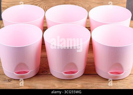 Empty pink plastic flower pots with trays on wooden background. Close-up. Stock Photo