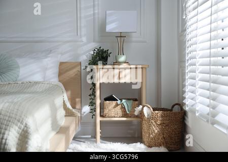 Bedside table with lamp and other decor near bed indoors Stock Photo