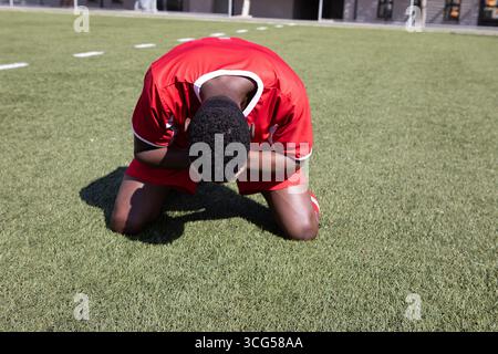 African American man soccer player kneeling holding head on green turf with white markings Stock Photo