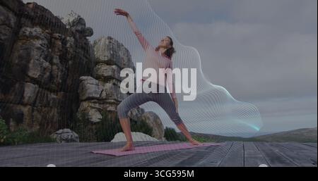 Stretching woman in pink top and leggings practicing yoga on deck, with pink yoga mat Stock Photo