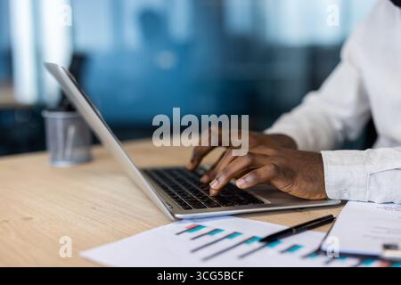 Professional workspace featuring a person typing on a laptop with charts and documents. The setting suggests focus, productivity, and data analysis within a modern business environment. Stock Photo