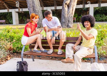 Young friends using smartphones and laughing together on a bench in a park Stock Photo