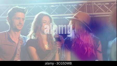 Laughing group wearing shirt and hat on stage under colored haze, with microphone and guitar strap Stock Photo