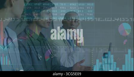 Three doctors wearing scrubs and lab coats examining charts in conference room, with stethoscopes Stock Photo