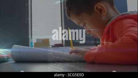 Writing boy wearing red hoodie focusing at home desk, using yellow pencil on notebook, copy space Stock Photo