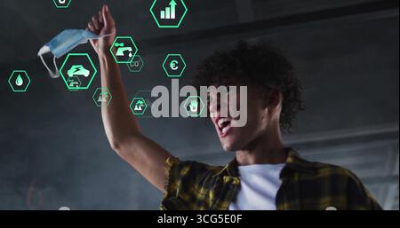 Shouting man wearing plaid shirt holding mask in industrial hall with holographic icons, copy space Stock Photo