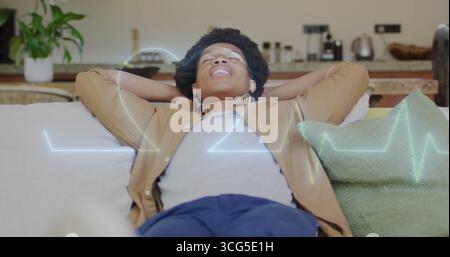 Reclining man holding hands behind head on living room sofa, with wireless earbuds and waveform Stock Photo