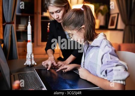 Modern mature woman helping her teen daughter with astronomy homework telling about stars in evening at home Stock Photo