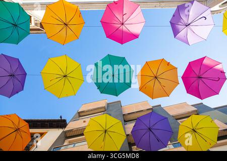 Multi-colored umbrellas hang on the street along the houses against the sky. Stock Photo