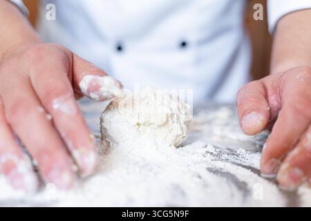 Bavaria, Germany - August 26, 2025: A baker kneads fresh dough with his hands on a floured work surface. Craftsmanship, tradition and passion combine in the art of baking to produce bread and pastries *** Ein Bäcker knetet mit den Händen frischen Teig auf einer bemehlten Arbeitsfläche. Handwerk, Tradition und Leidenschaft verbinden sich in der Backkunst zur Herstellung von Brot und Gebäck Stock Photo