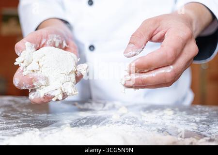 Bavaria, Germany - August 26, 2025: A baker kneads fresh dough with his hands on a floured work surface. Craftsmanship, tradition and passion combine in the art of baking to produce bread and pastries *** Ein Bäcker knetet mit den Händen frischen Teig auf einer bemehlten Arbeitsfläche. Handwerk, Tradition und Leidenschaft verbinden sich in der Backkunst zur Herstellung von Brot und Gebäck Stock Photo