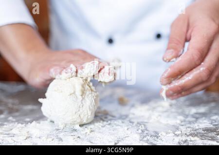 Bavaria, Germany - August 26, 2025: A baker kneads fresh dough with his hands on a floured work surface. Craftsmanship, tradition and passion combine in the art of baking to produce bread and pastries *** Ein Bäcker knetet mit den Händen frischen Teig auf einer bemehlten Arbeitsfläche. Handwerk, Tradition und Leidenschaft verbinden sich in der Backkunst zur Herstellung von Brot und Gebäck Stock Photo