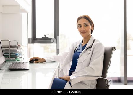Positive confident young female practitioner doctor sitting at workplace Stock Photo