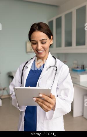 Happy young 30s doctor woman in lab coat using tablet Stock Photo