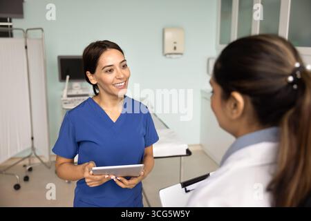 Positive doctor woman in blue scrubs talking to female coworker Stock Photo