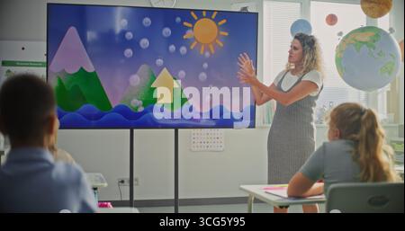 Elementary School Students Studying Basic Information About Weather Factors in Modern Classroom. Female Teacher Explaining Water Cycles to Smart Kids During Geography Lesson Using Digital Screen. Stock Photo