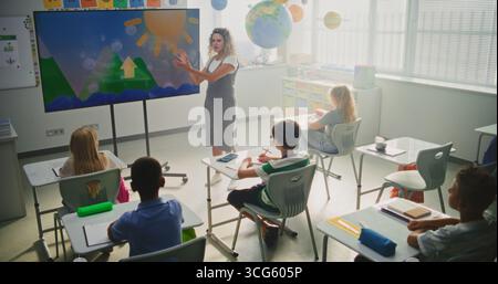 Elementary School Students Studying Basic Information About Weather Factors in Modern Classroom. Female Teacher Explaining Water Cycles to Smart Kids During Geography Lesson Using Digital Screen. Stock Photo