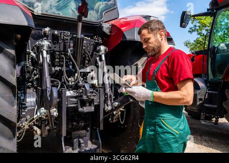 Man farm worker checking farm tractor using digital tablet in rural area Stock Photo