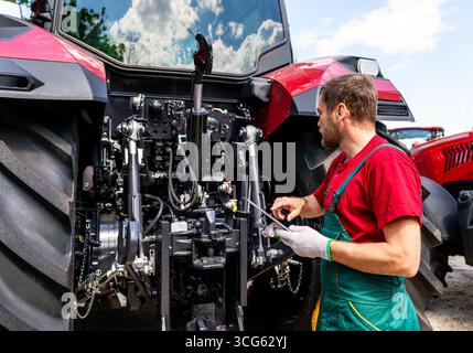 Male mechanic checking farm tractor using digital tablet in rural area Stock Photo
