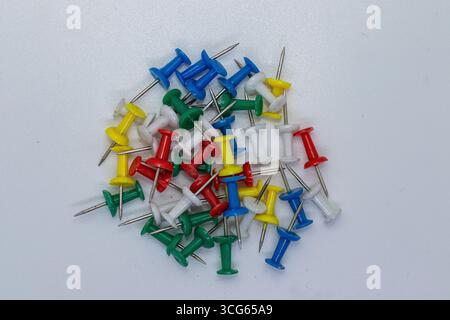 Collection of colorful push pins in green, red, blue, yellow, and white, scattered on a neutral surface. Essential stationery items for pinning notes, Stock Photo