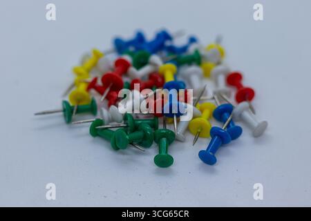 Colorful plastic push pins scattered on a white background. Essential office and school stationery items used for pinning papers, notes, or reminders Stock Photo