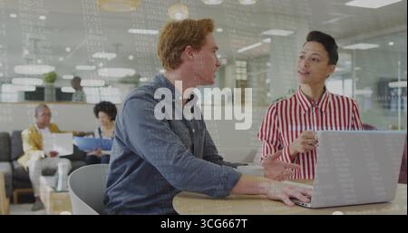 Collaborating White man and female colleague working on laptop at office lounge, with notebooks Stock Photo