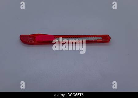 Compact red stationery cutter knife with retractable blade, ideal for cutting paper, cardboard, and packaging. Office and school utility tool on white Stock Photo