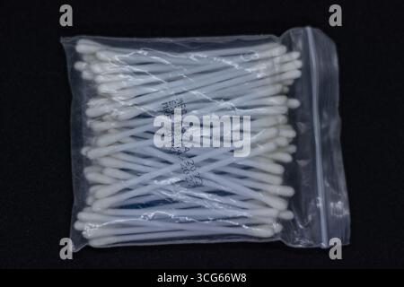 Cotton ear buds stored in a clear plastic container on a black background. Clean hygiene product, ideal for personal care, skincare, and medical use. Stock Photo