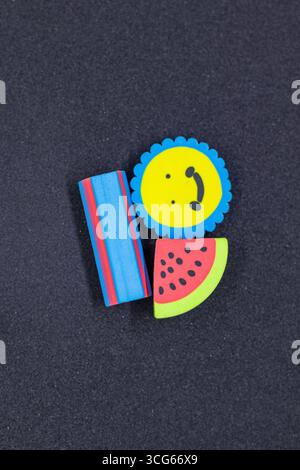 Colorful fruit-shaped and smiley face erasers arranged on a dark background. Fun stationery for kids, school supplies, and creative learning tools. Br Stock Photo