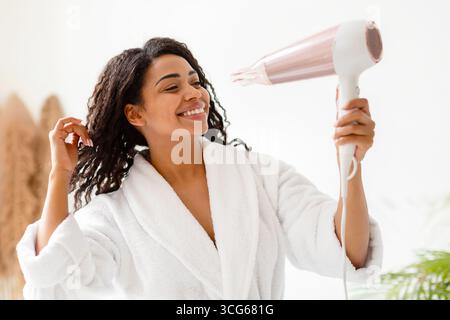 Happy Black Woman Drying Curly Hair With Hairdryer In Bathroom Stock Photo