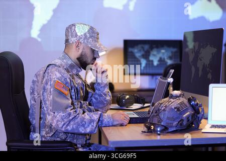 Thoughtful soldier working with military laptop on table in office at night Stock Photo