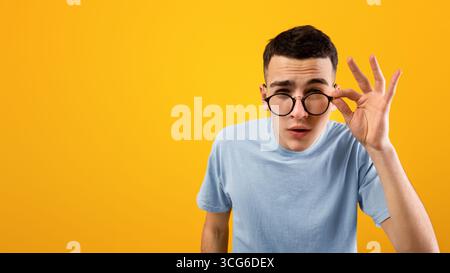 Young Caucasian man in glasses being skeptical, looking suspicious, having some doubt on orange studio background Stock Photo