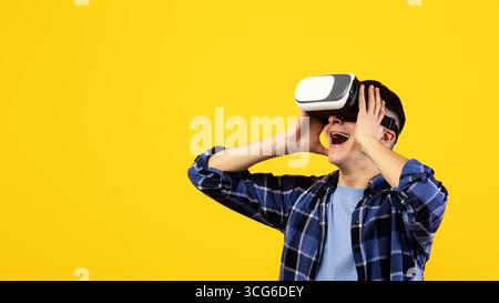 Cheerful young man in virtual reality glasses playing online game, feeling excited on orange studio background Stock Photo