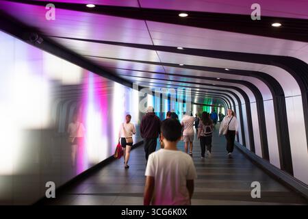Commuters walk through the colorful, futuristic light tunnel at London's King's Cross Station, connecting to various train lines. Stock Photo