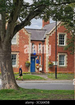 Traditional red brick police station in Sedgefield, County Durham, with flower baskets, blue door, and a man walking along a quiet street Stock Photo